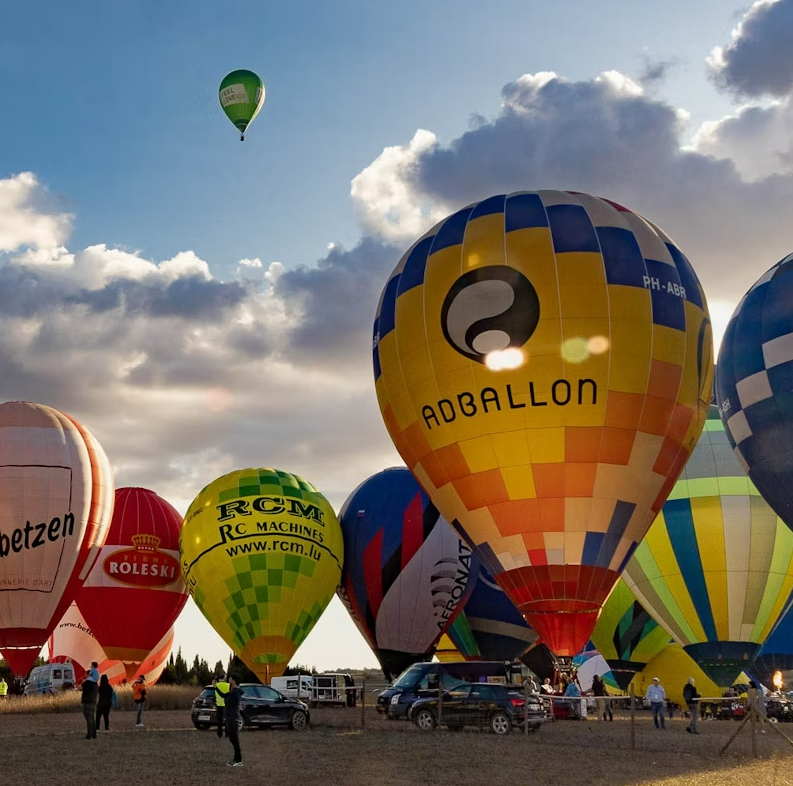 A group of colorful hot air balloons prepares for takeoff at sunrise