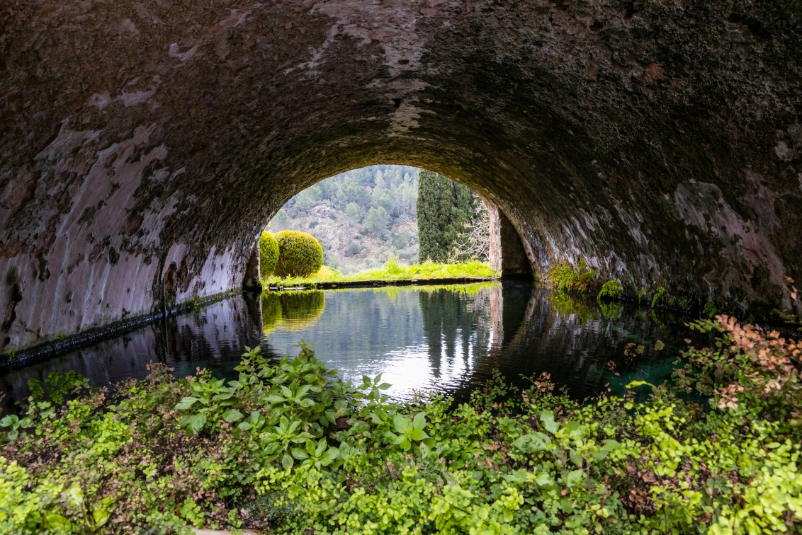 A peaceful water reflection under a historic stone arch in Jardines de Alfabia